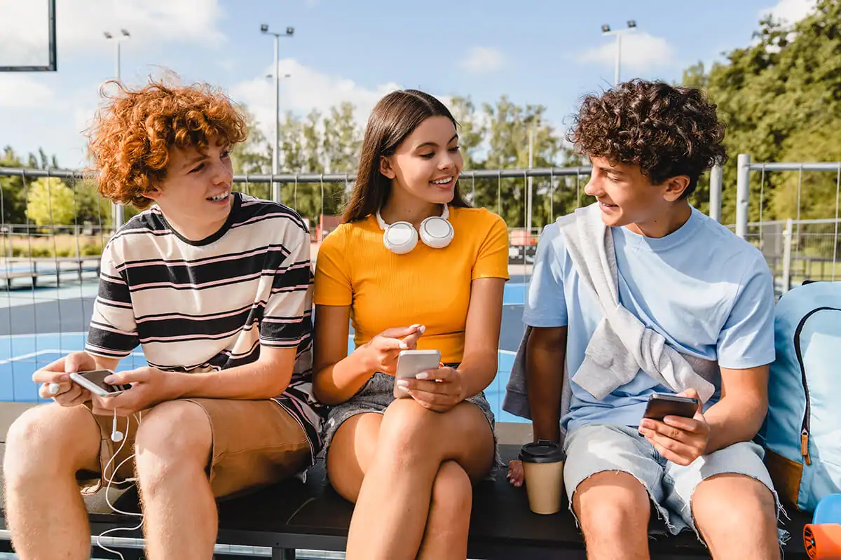 Three teens sitting together smiling and holding smartphones