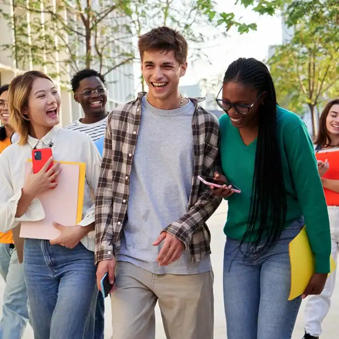 A group of teens laughing together while holding smartphones at school