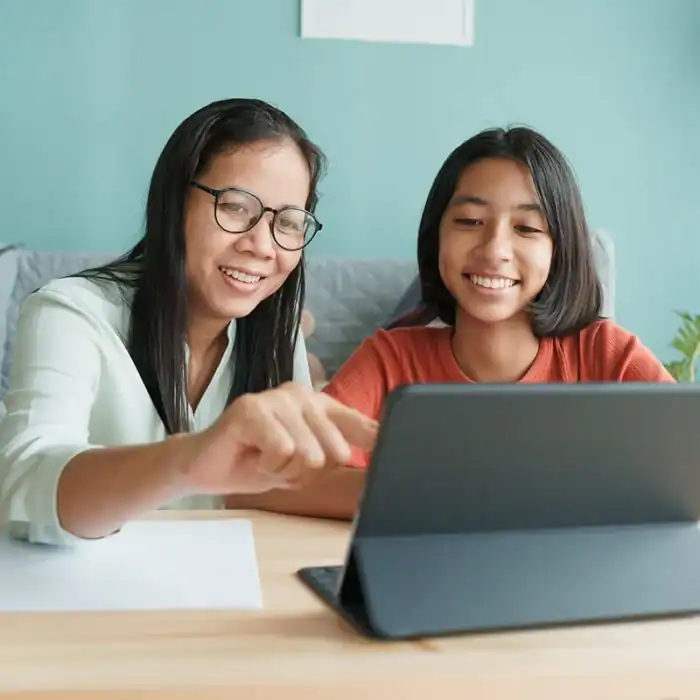 Mother and daughter smiling while using a tablet together at home