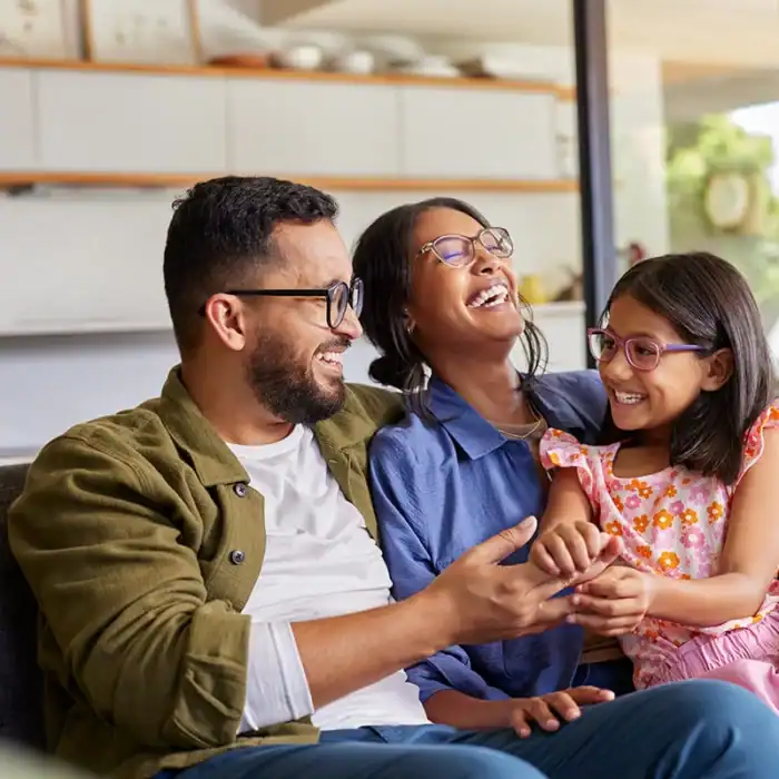 Mother, father and daughter laughing together at home on a couch