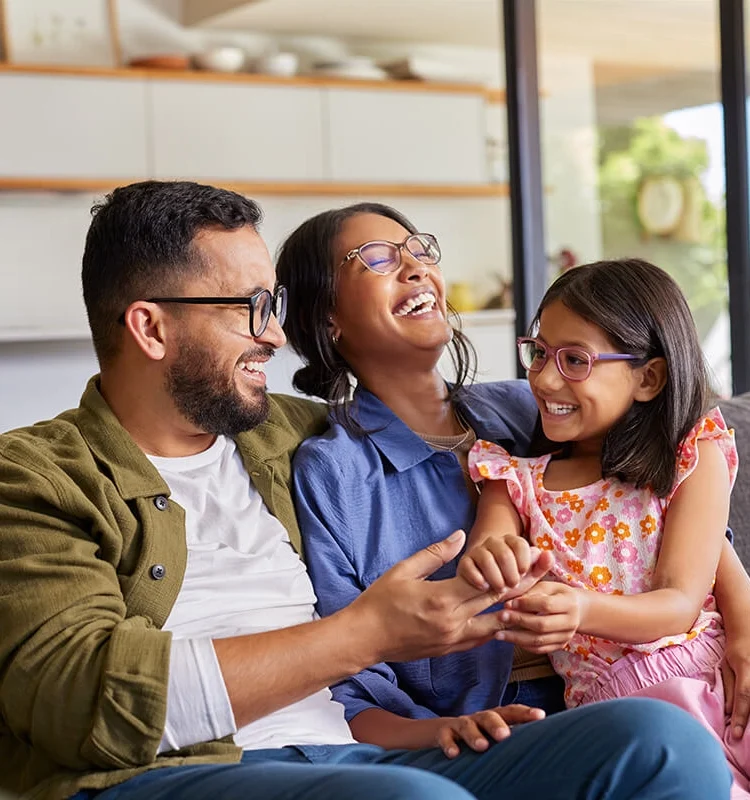 Mother, father and daughter laughing together at home on a couch