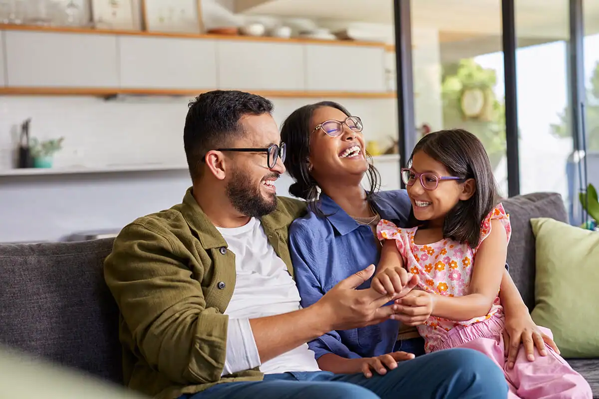 Mother, father and daughter laughing together at home on a couch