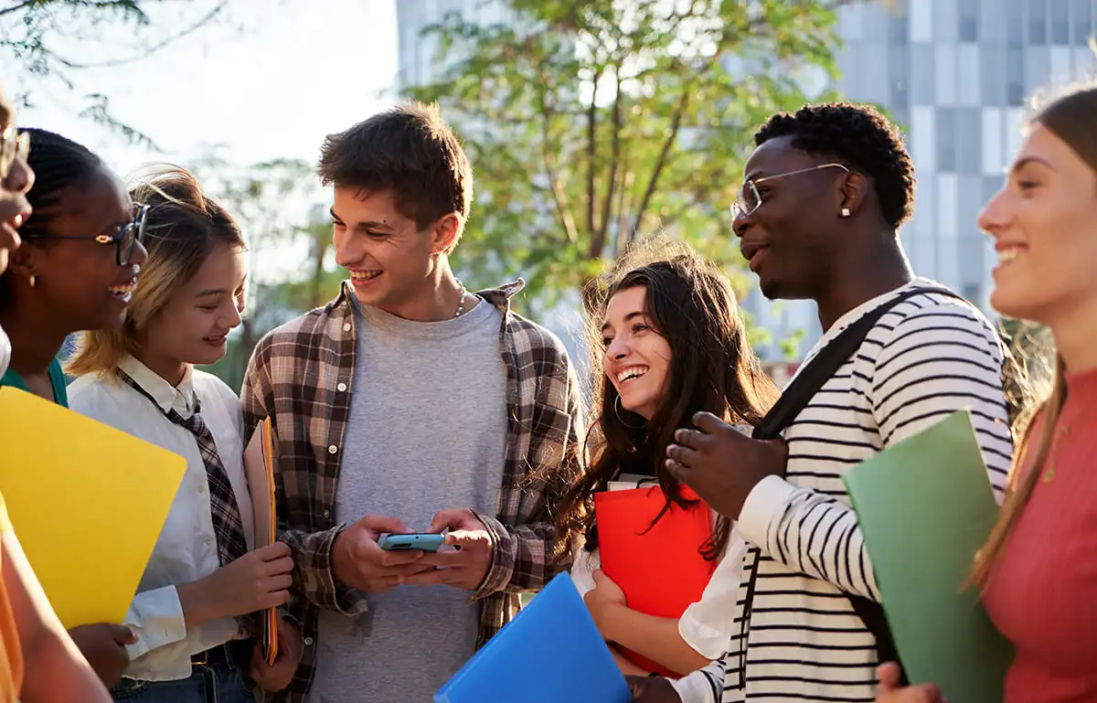 Group of teen students smiling, including one holding a smartphone