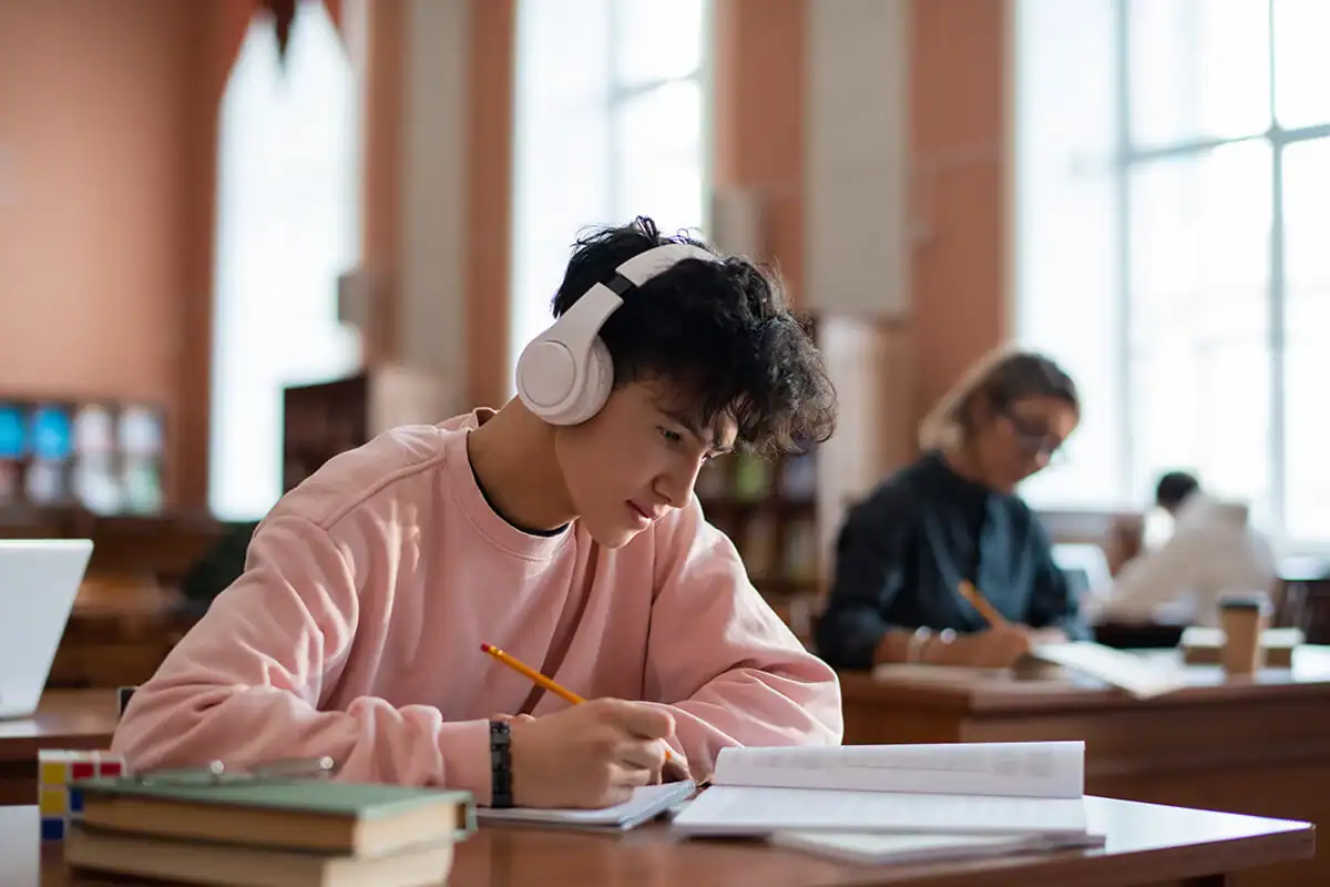Teen student wearing headphones while doing homework in a library