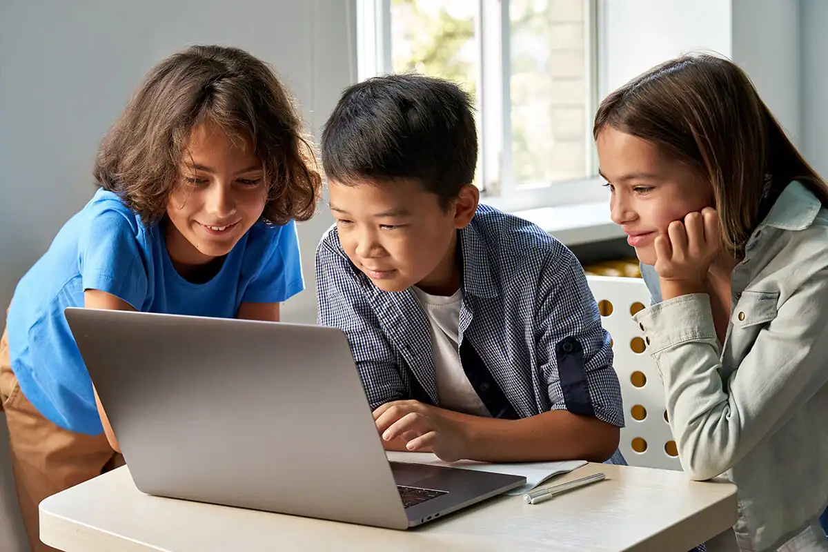 Three children smiling while looking at a laptop computer