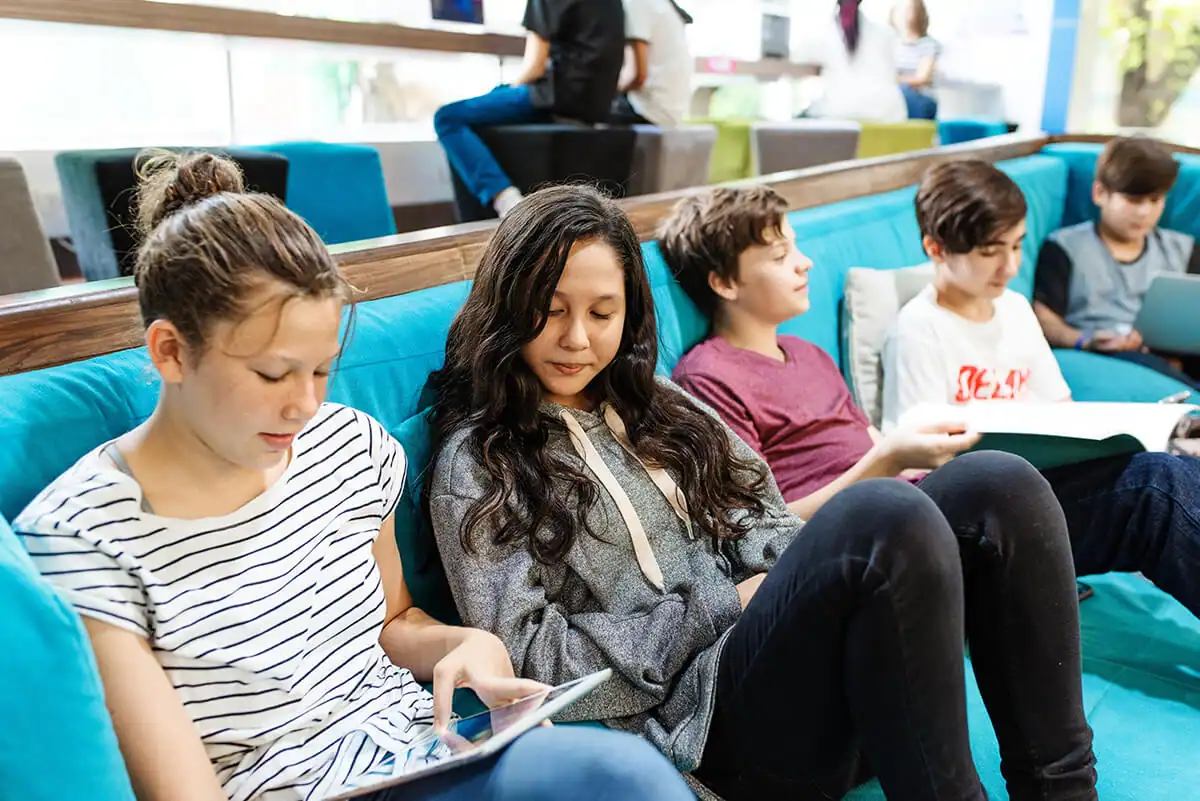 Students lounging on a couch with books and tablets