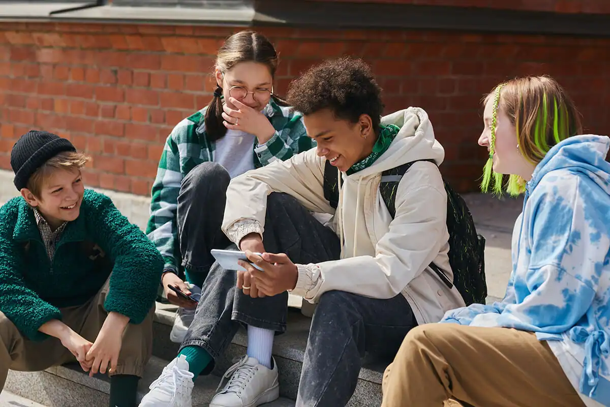 Four students laughing while looking at a smartphone