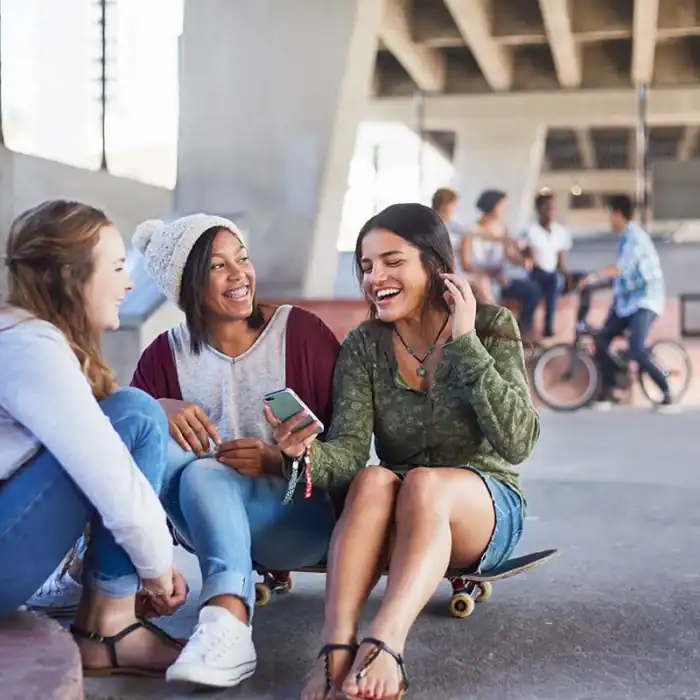 Three students at a skate park smiling and looking at a smartphone