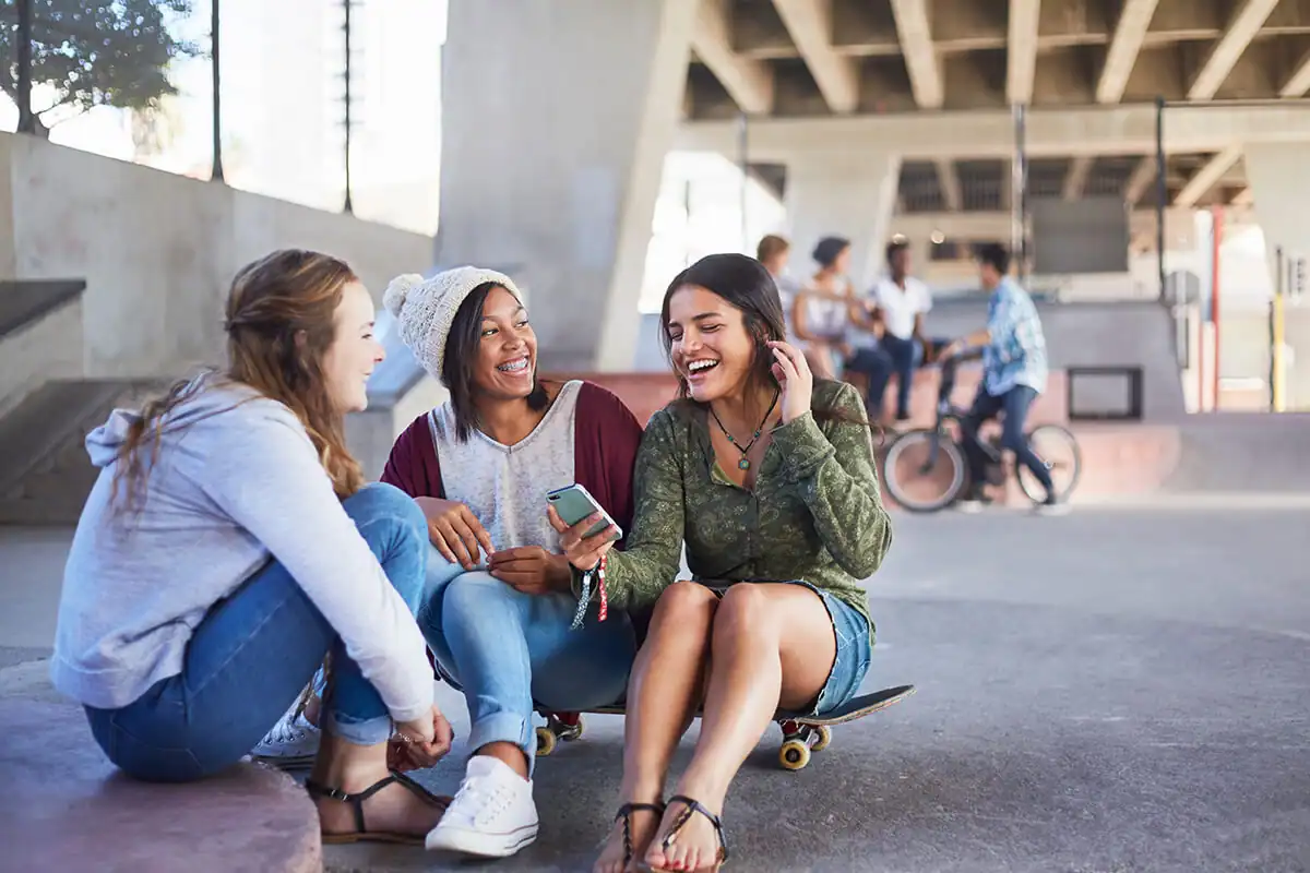 Three students at a skate park smiling and looking at a smartphone
