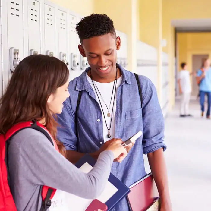 Two students in a school hallway smiling while looking at a smartphone