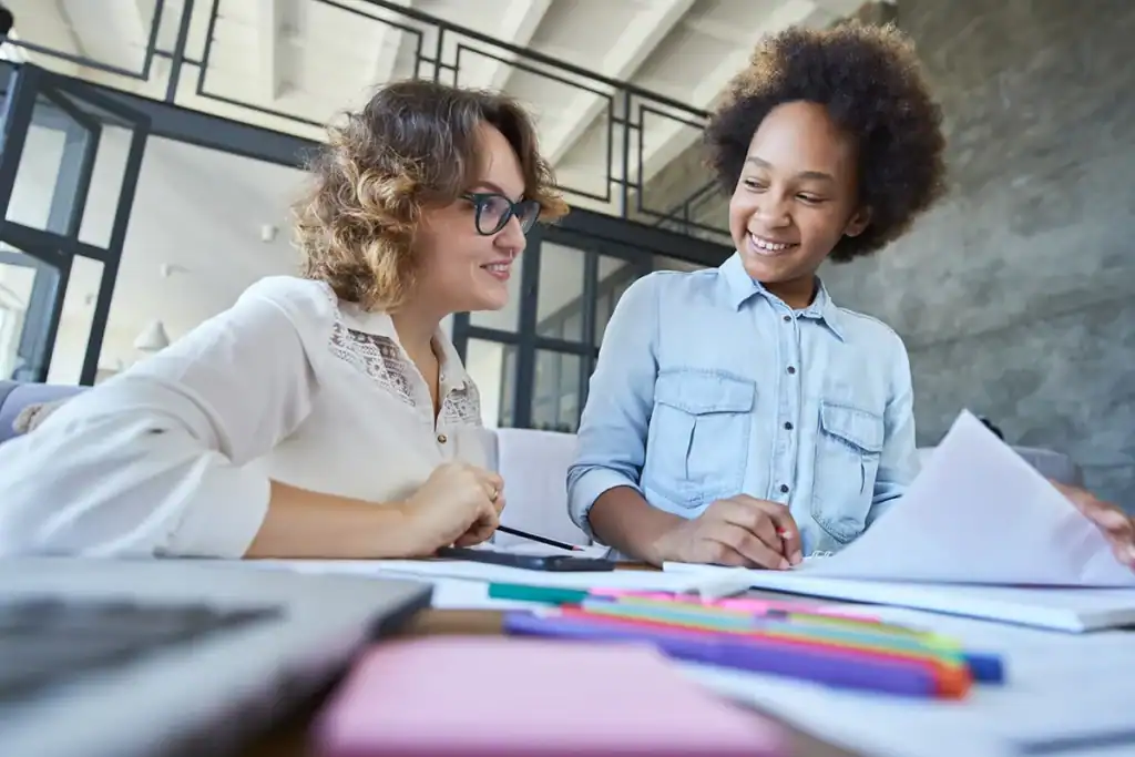 Adult and student smiling while working on schoolwork together